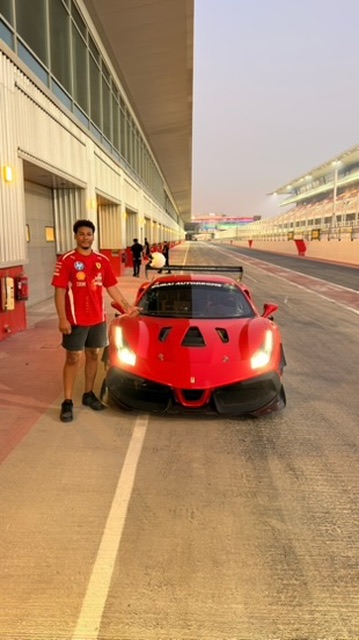 Shawn standing beside a red Ferrari race car in pit lane